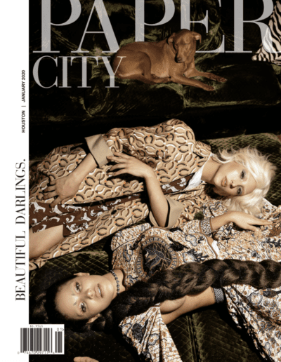 Two women posing for a fashion magazine cover with a dog, dressed in patterned outfits.