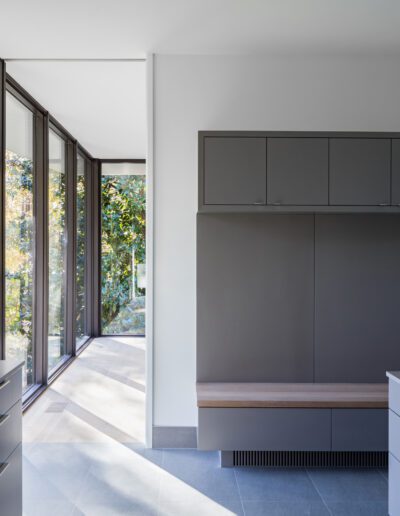 Minimalist interior with gray cabinets, two countertops, and large floor-to-ceiling windows showing outdoor trees. Bright natural light fills the space.