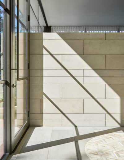 Sunlight casts shadows through a window onto a beige tiled wall and floor, creating sharp geometric patterns in an indoor space.