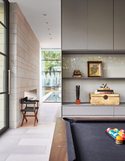 Modern room with pool table, glass door opening to garden, shelves with decor items and bar set.