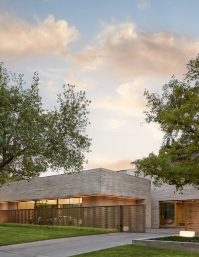 Modern, single-story house with wooden exterior, surrounded by trees and a neatly landscaped lawn. Twilight sky in the background.