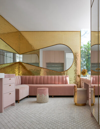 A modern living room with pink couches, a geometric-patterned floor, and gold mirrored walls.