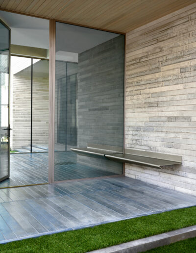 Modern corner of a building with glass walls, a smooth stone bench, and blue tile flooring.