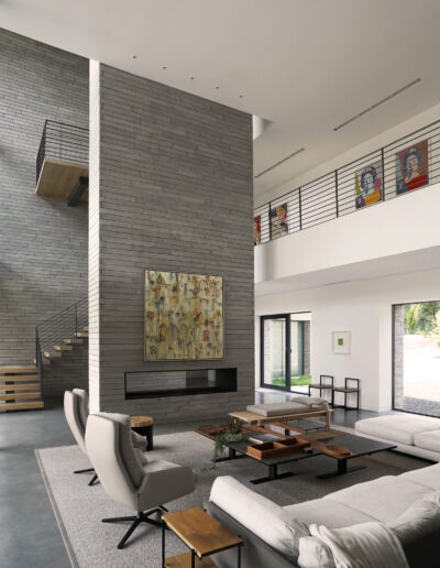 Modern living room with high ceilings, a central fireplace, and a mezzanine with glass balustrades.