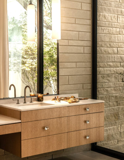 Modern bathroom with a floating wooden vanity, single sink, two pendant lights, large mirror, and textured beige tile walls.